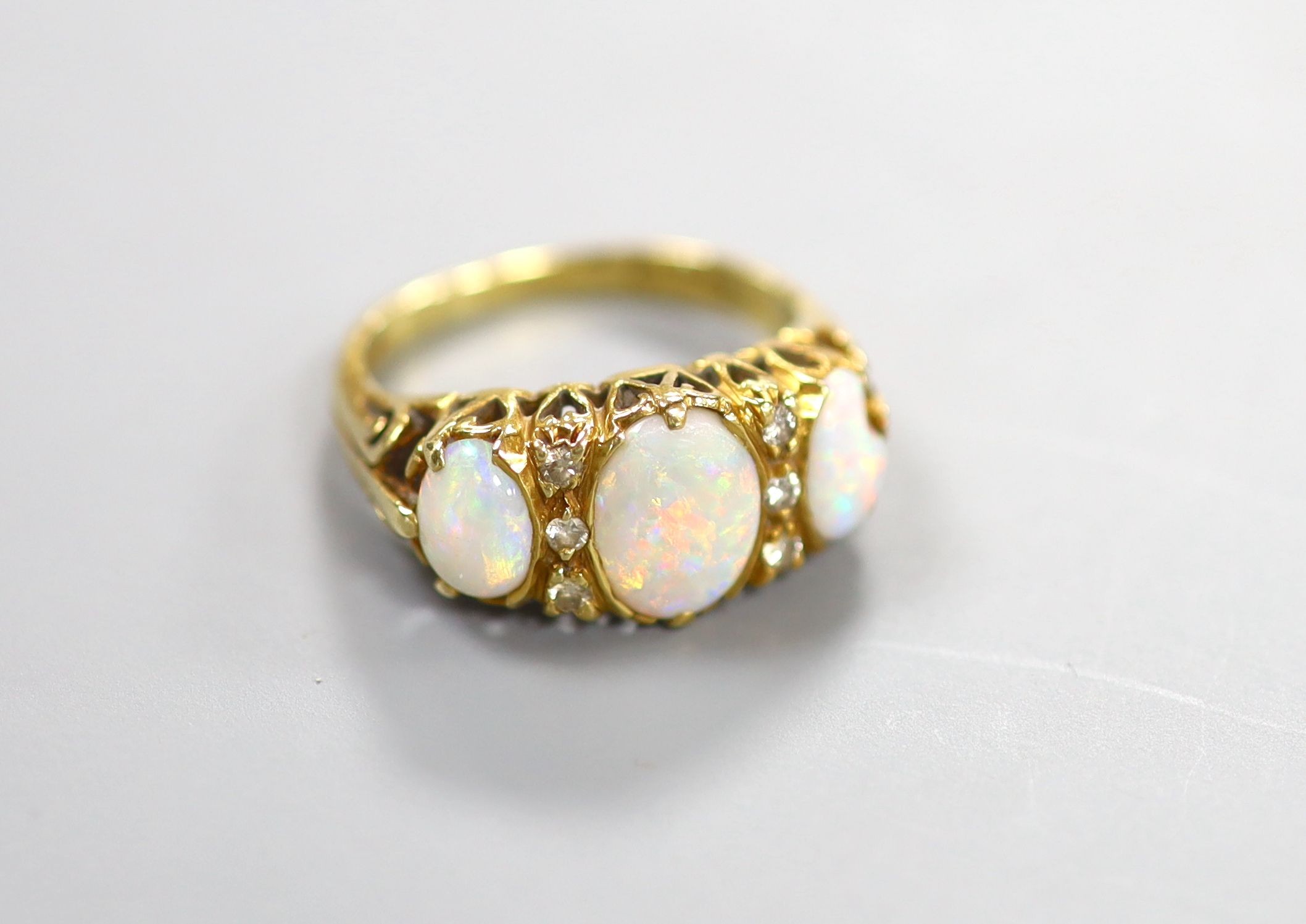 A 1970's Victorian style 18ct gold and graduated three stone white opal half hoop ring, with diamond chip spacers, size N, gross weight 5.9 grams.